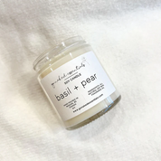 Soy candle labeled 'basil + pear' on a white fabric background