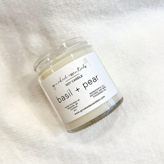 Soy candle labeled 'basil + pear' on a white fabric background