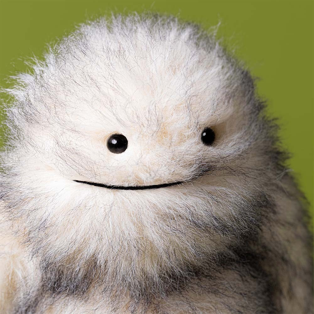 close up of Yeti Plush Toy by Jellycat with fluffy grey & white fur on green background