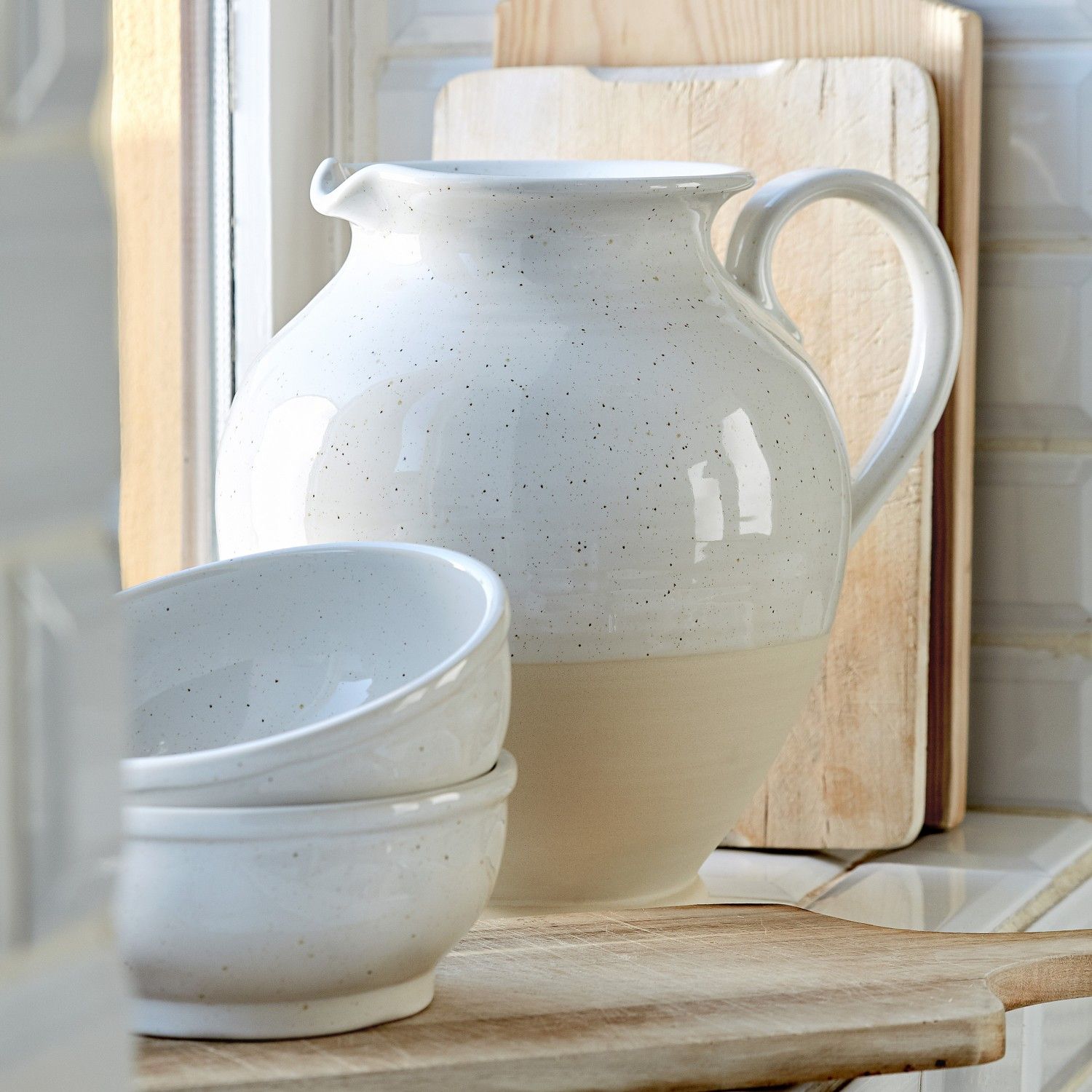 White ceramic pitcher and bowls on a wooden surface with a tiled wall background