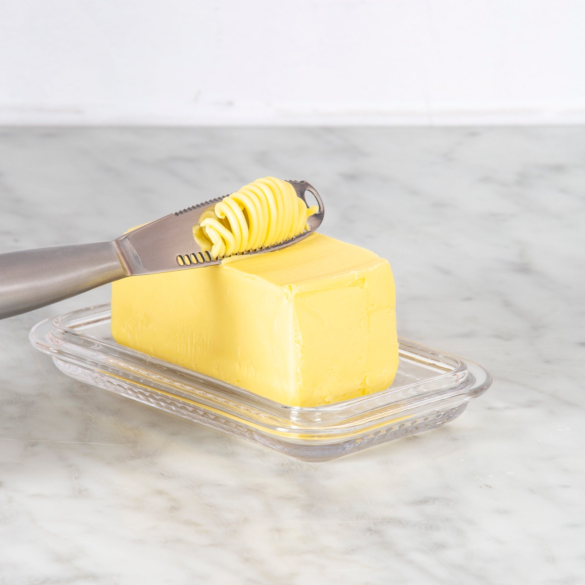 Butter dish with a stick of butter and a knife on a marble surface