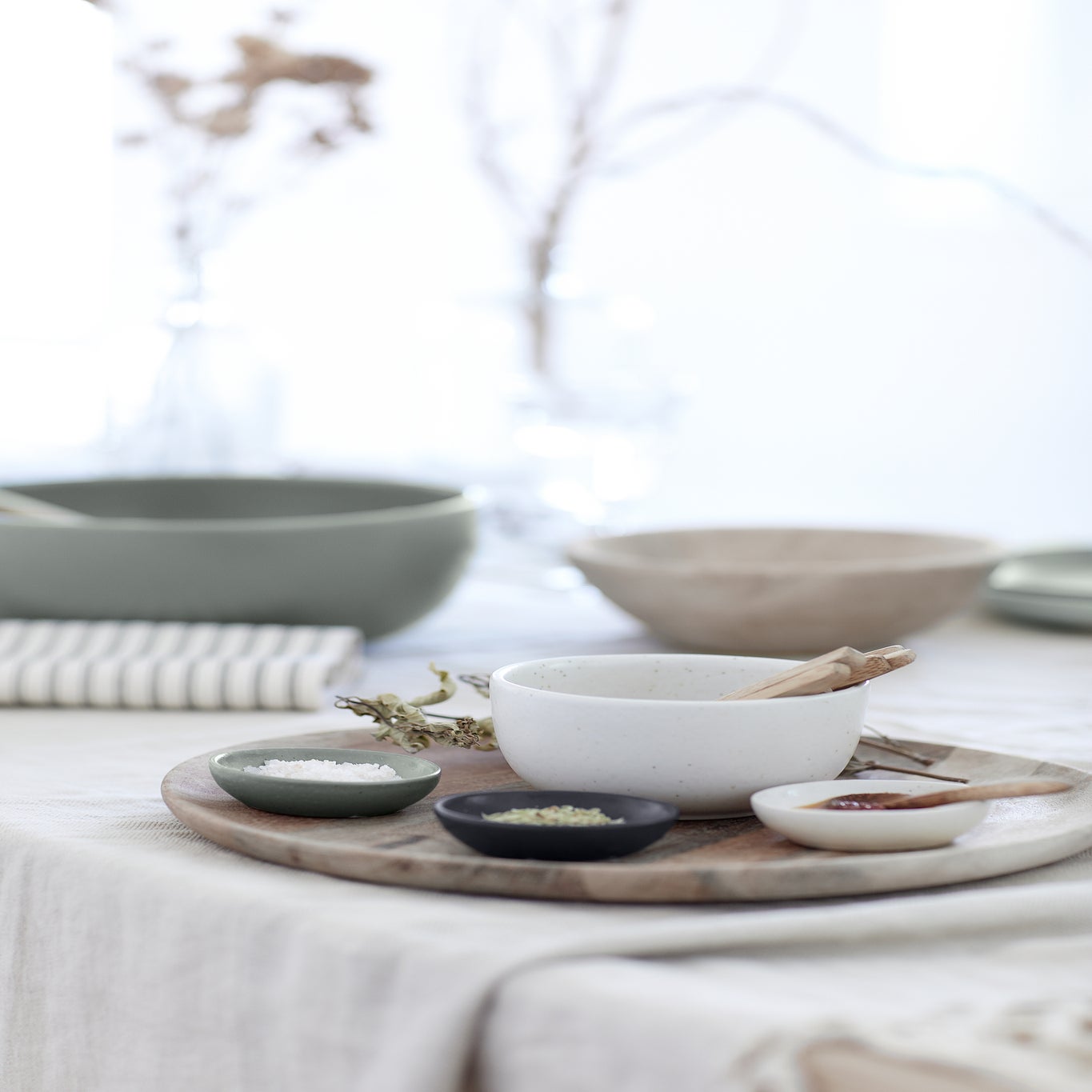 Table setting with ceramic bowls and a wooden tray on a light surface.