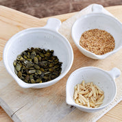 Three small white measuring bowls with seeds on a wooden surface