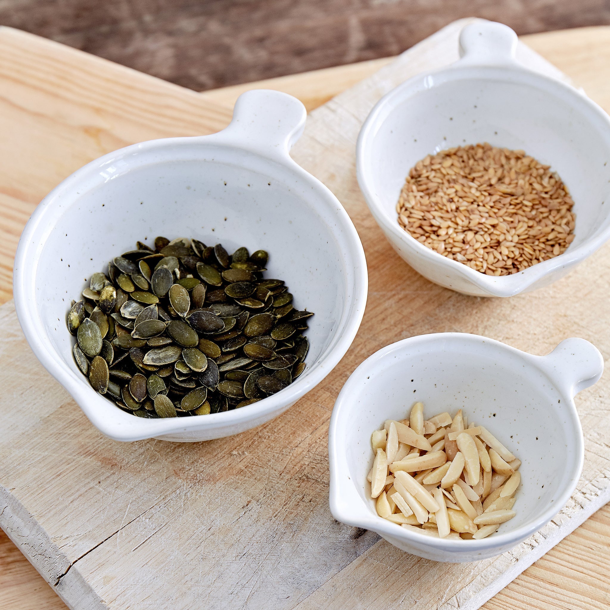 Three small white measuring bowls with seeds on a wooden surface