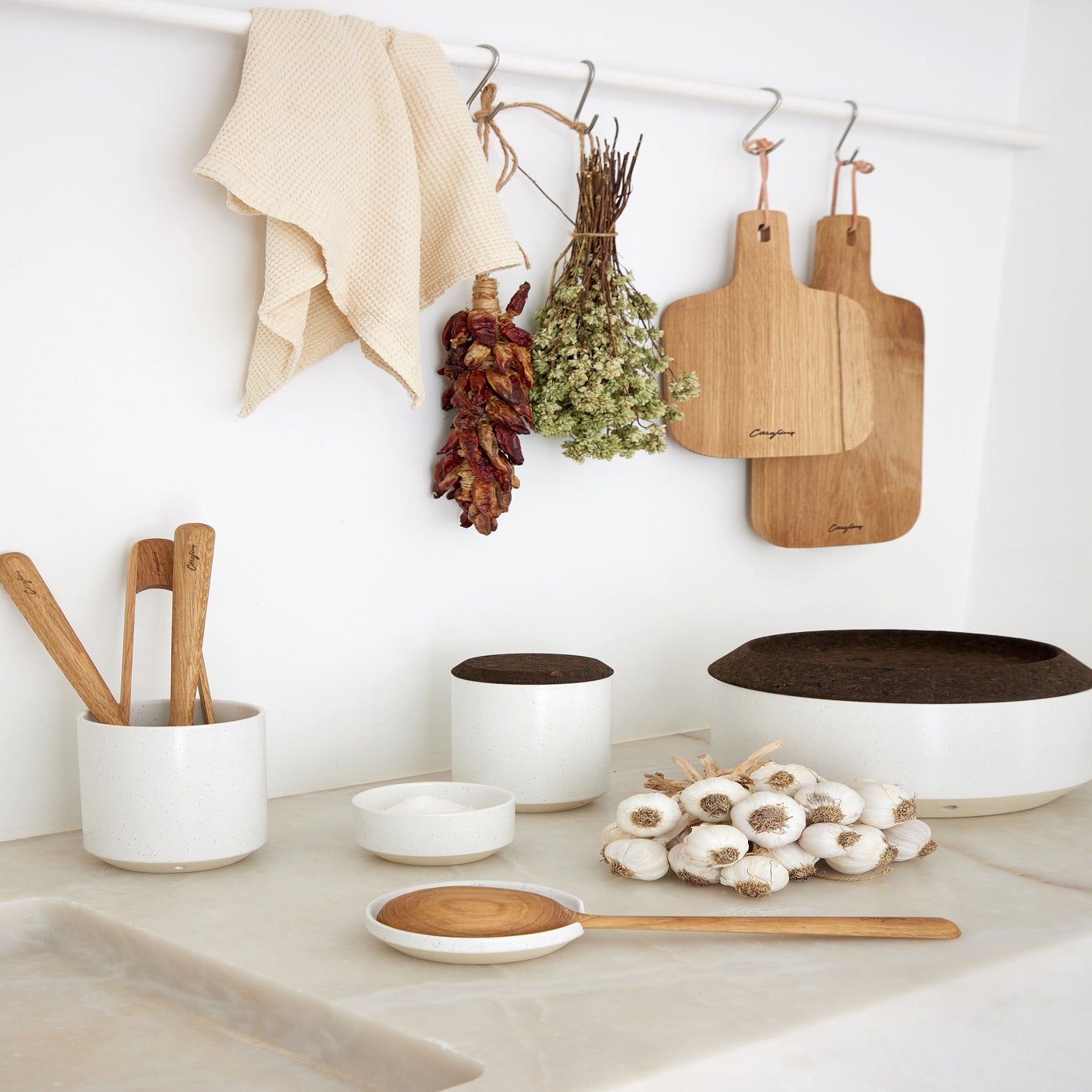 Kitchen counter with wooden utensils, cutting boards, and white containers against a white wall.