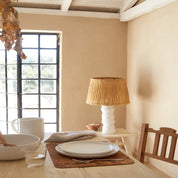 Dining room with a table set for a meal, lamp, and window in the background.