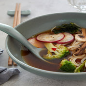 Bowl of soup with vegetables and noodles on a light surface