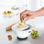 Person using a ginger grater on a white surface with ingredients around