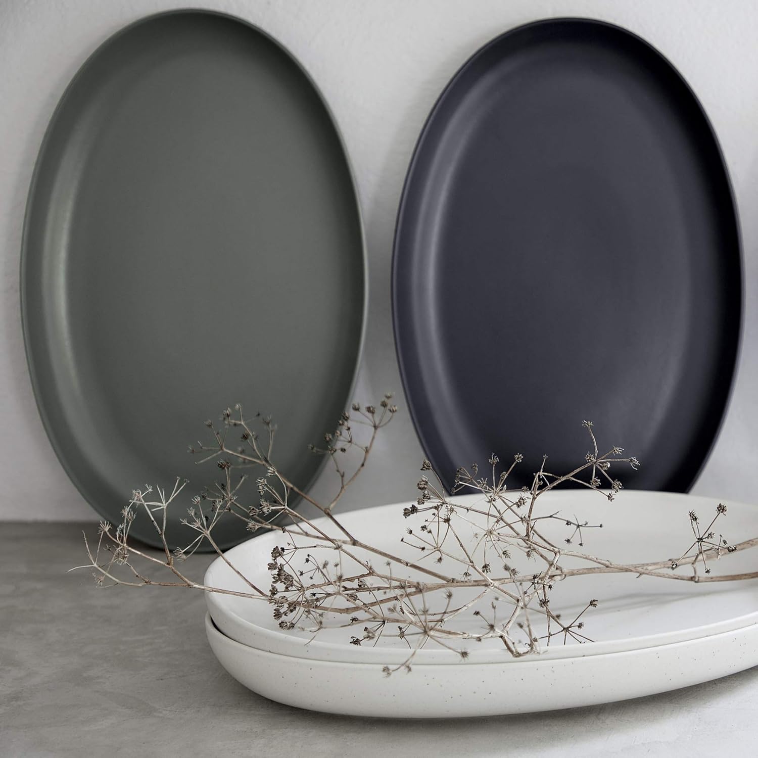 Three oval plates in gray, black, and white on a light gray surface with dried branches.