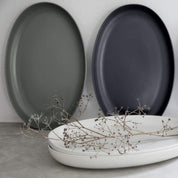 Three oval plates in gray, black, and white on a light gray surface with dried branches.