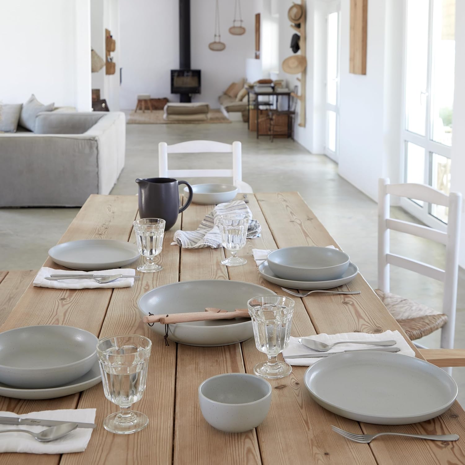 Dining table set with gray plates, glasses, and cutlery in a modern living room.
