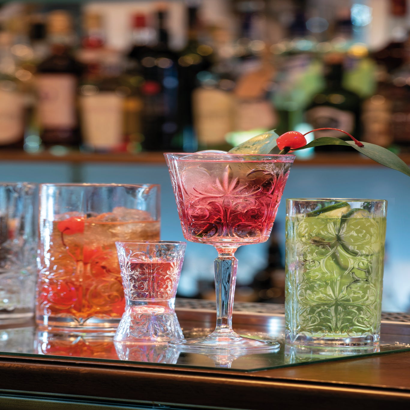Assorted cocktails on a bar with blurred bottles in the background