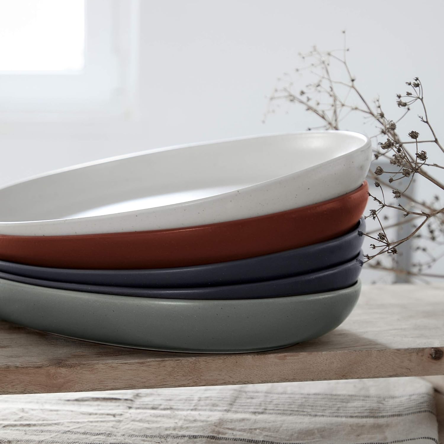 Stack of ceramic bowls in white, red, and gray on a wooden surface with a light background.