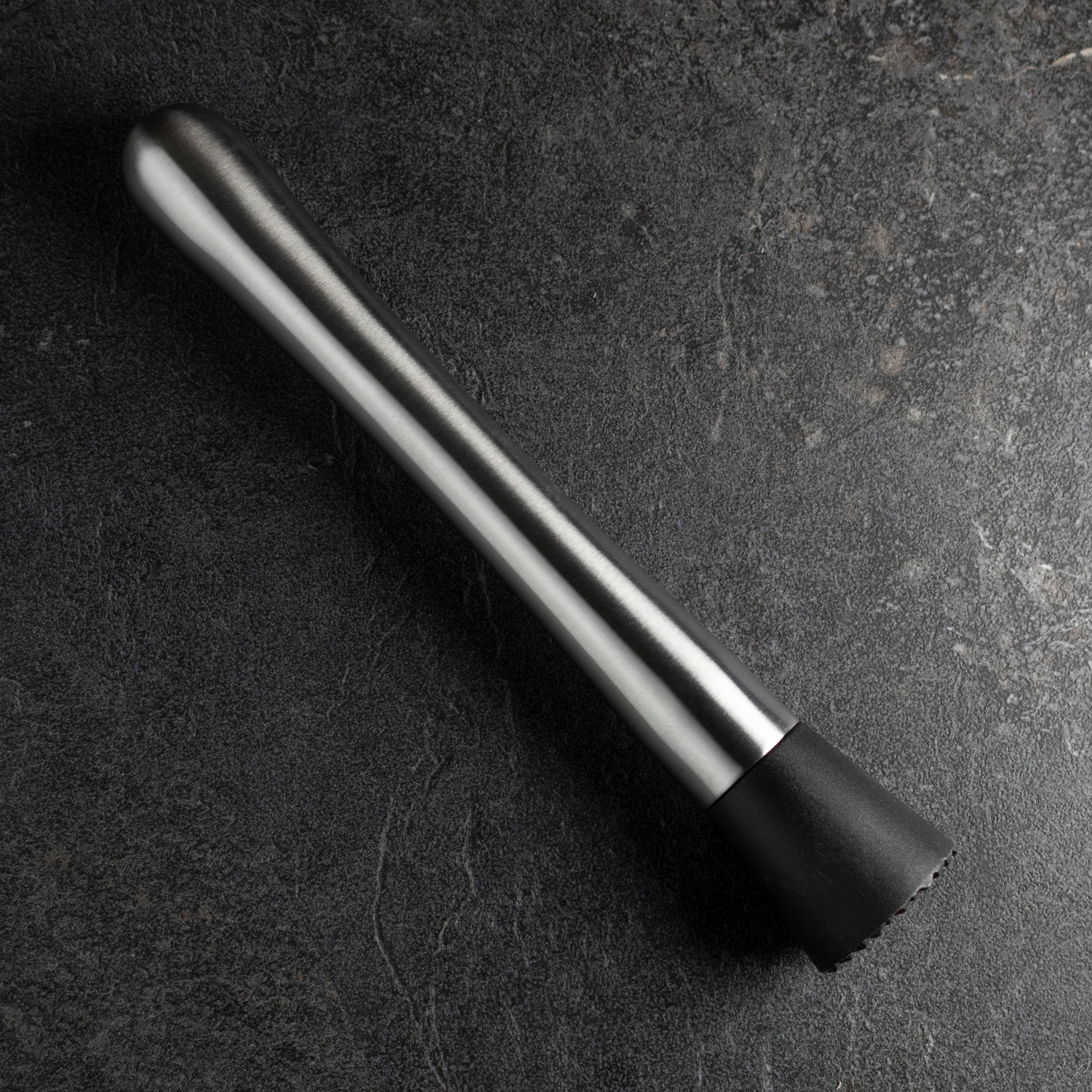 Black and silver cocktail muddler on a dark surface