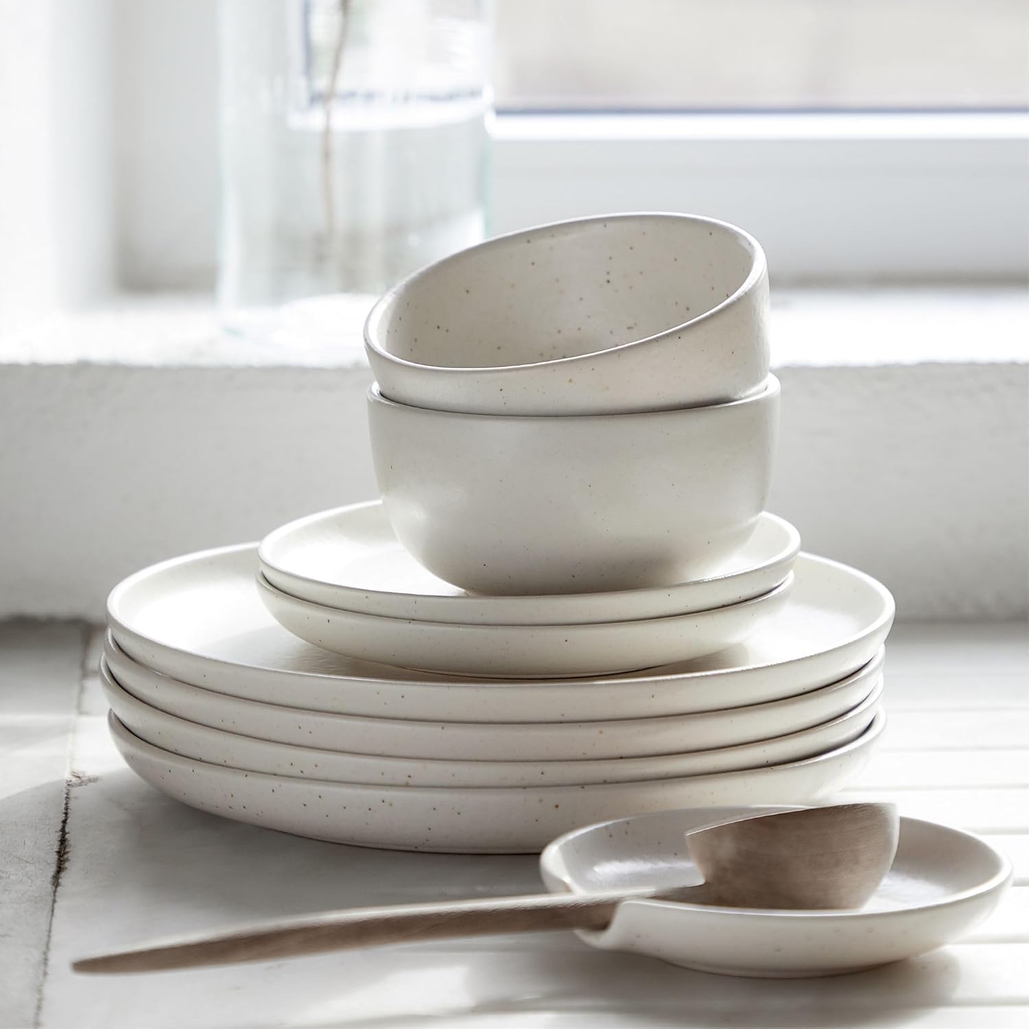 Set of white ceramic bowls and plates on a light surface with a blurred window background