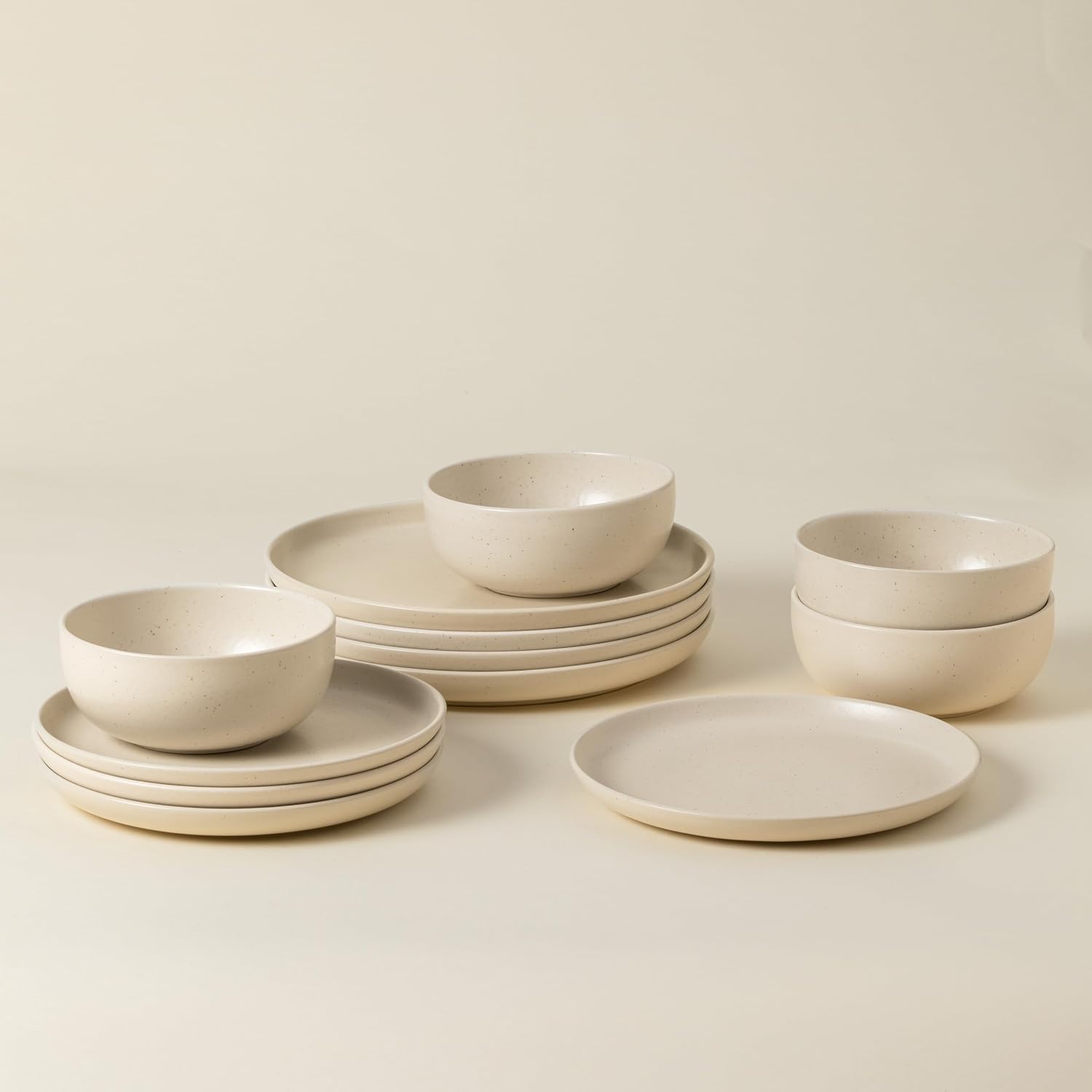 Set of beige ceramic dinnerware including bowls and plates on a light background