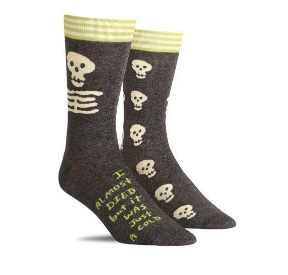 dark grey socks with cartoon skulls that says i almost dies but it was just a cold
