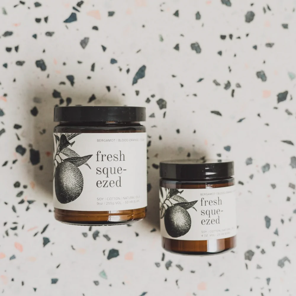 both fresh squeezed candle brown jar white label black lid on terrazzo style background