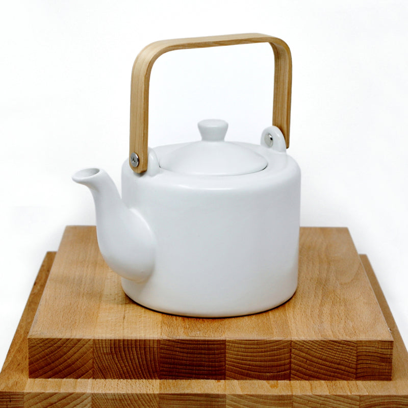 matte white teapot with wood handle and lid closed, on top of wood cutting boards