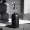 black wylie vase by everlasting candle co with three lit silver candle wicks inside on stone background