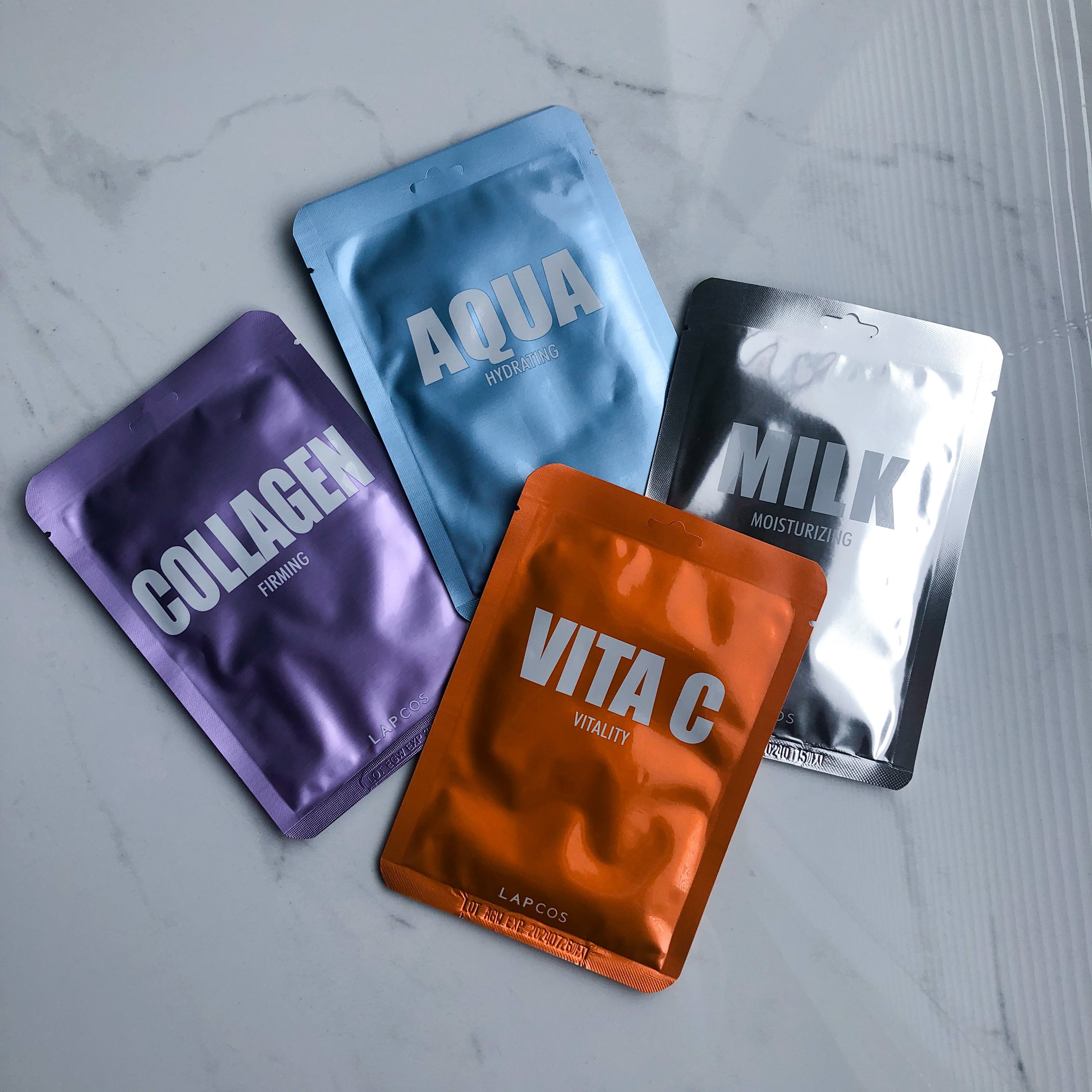 four shiny orange, silver, purple and blue facemask packages on marble counter by lapcos