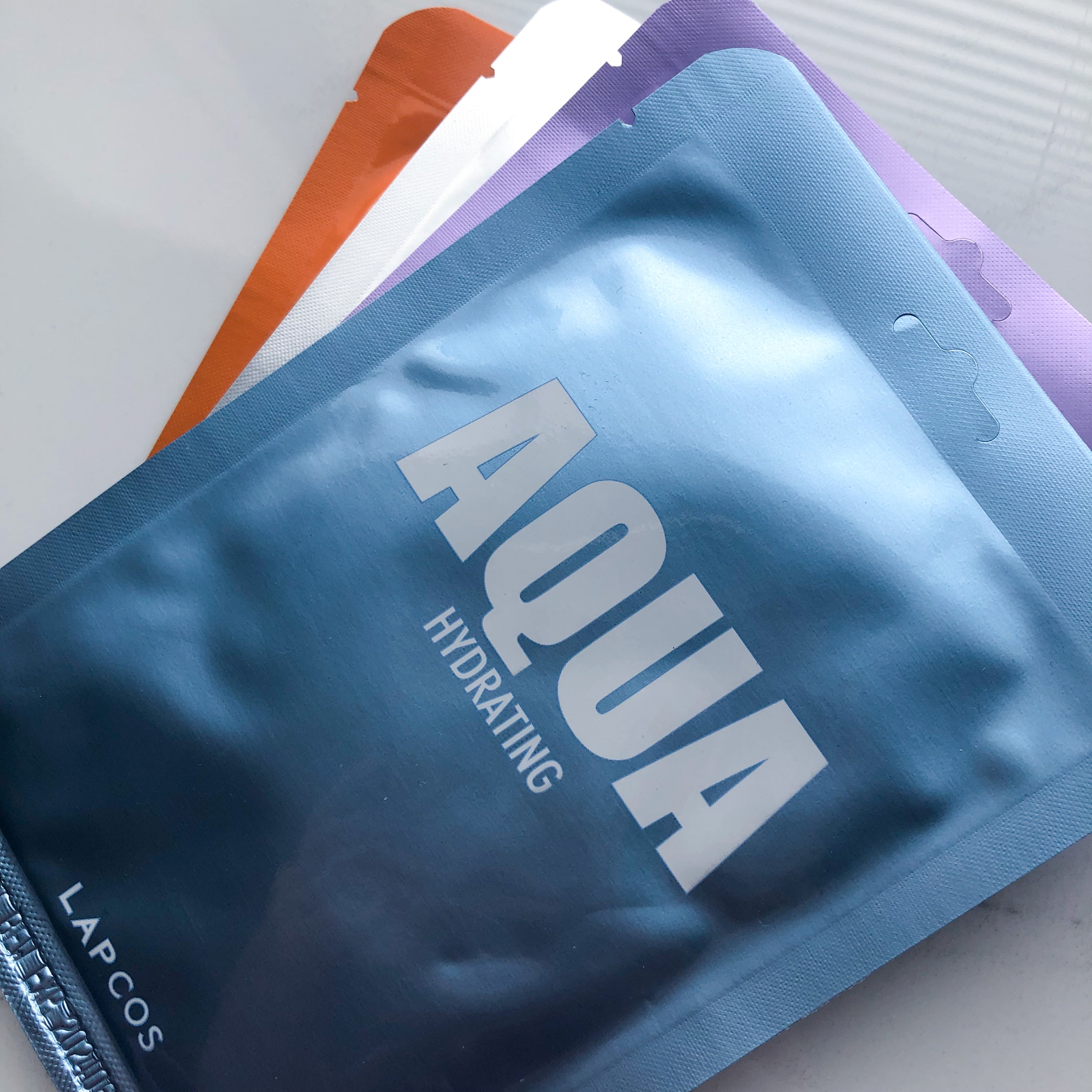 shiny blue 'aqua ' facemask package on top of 3 other masks  by lapcos