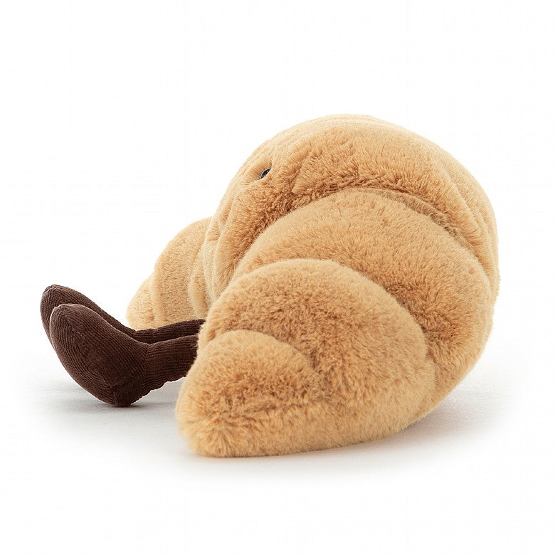 side view of fluffy brown croissant stuffed plush toy with black smiley face from jellycat