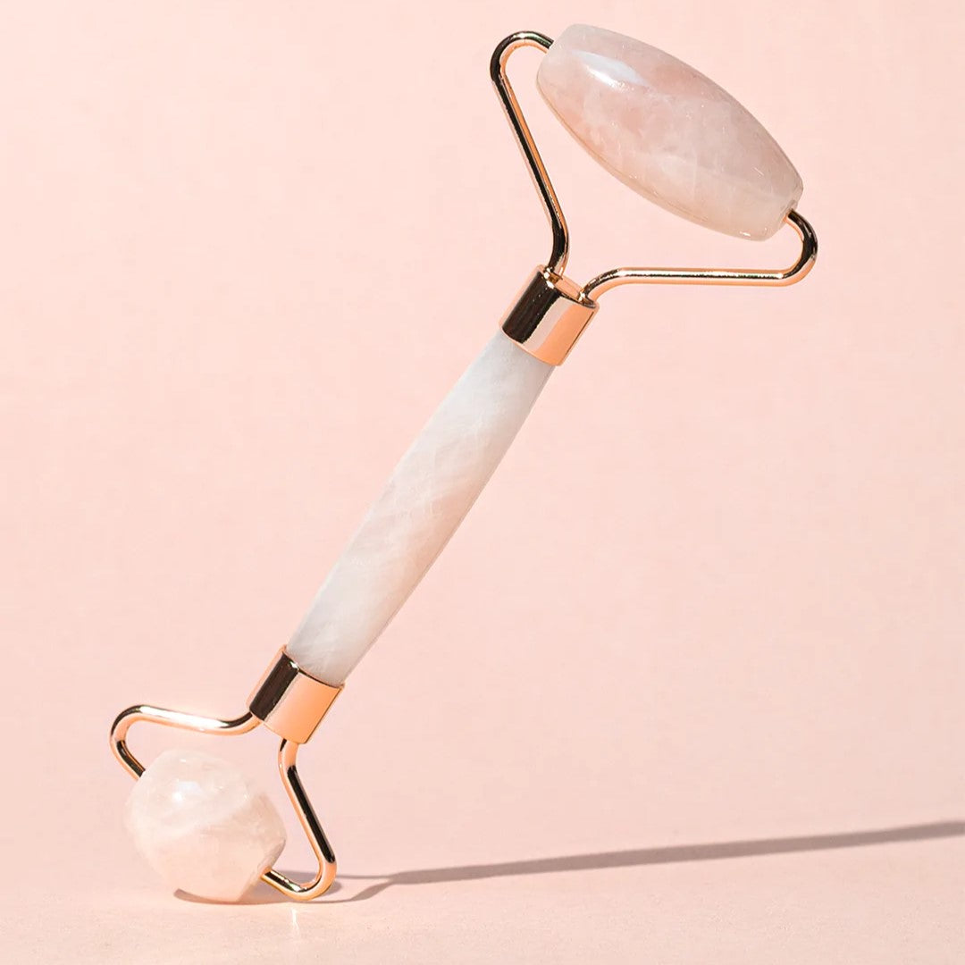 rose quartz and gold facial roller standing on edge with shadow on a pink background