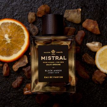 glass bottle with wood top of mistral for men eau de parfum cologne in scent black amber  with amber and oranges behind
