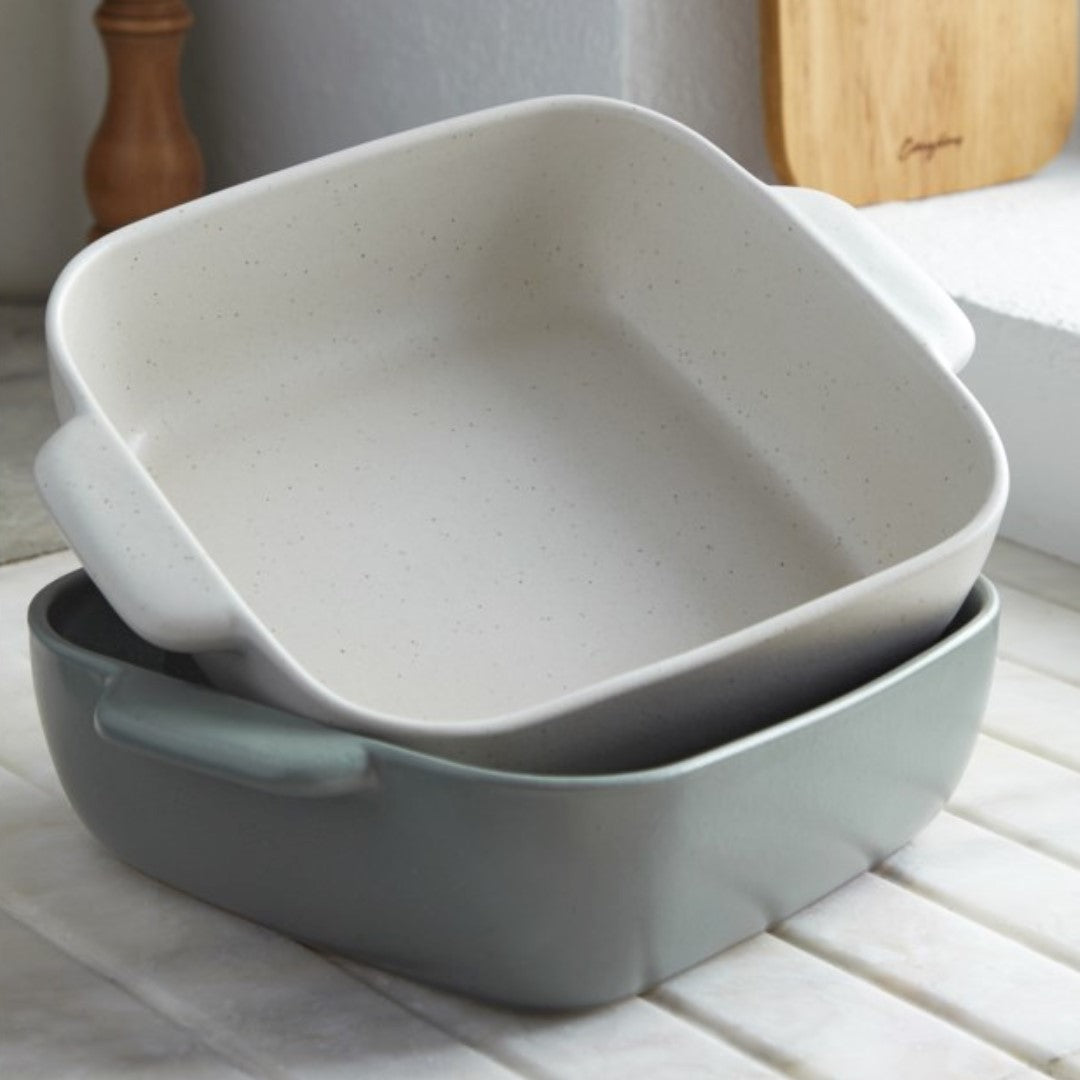 square off white speckled stoneware baking dish with handles on top of same style in green on white counter