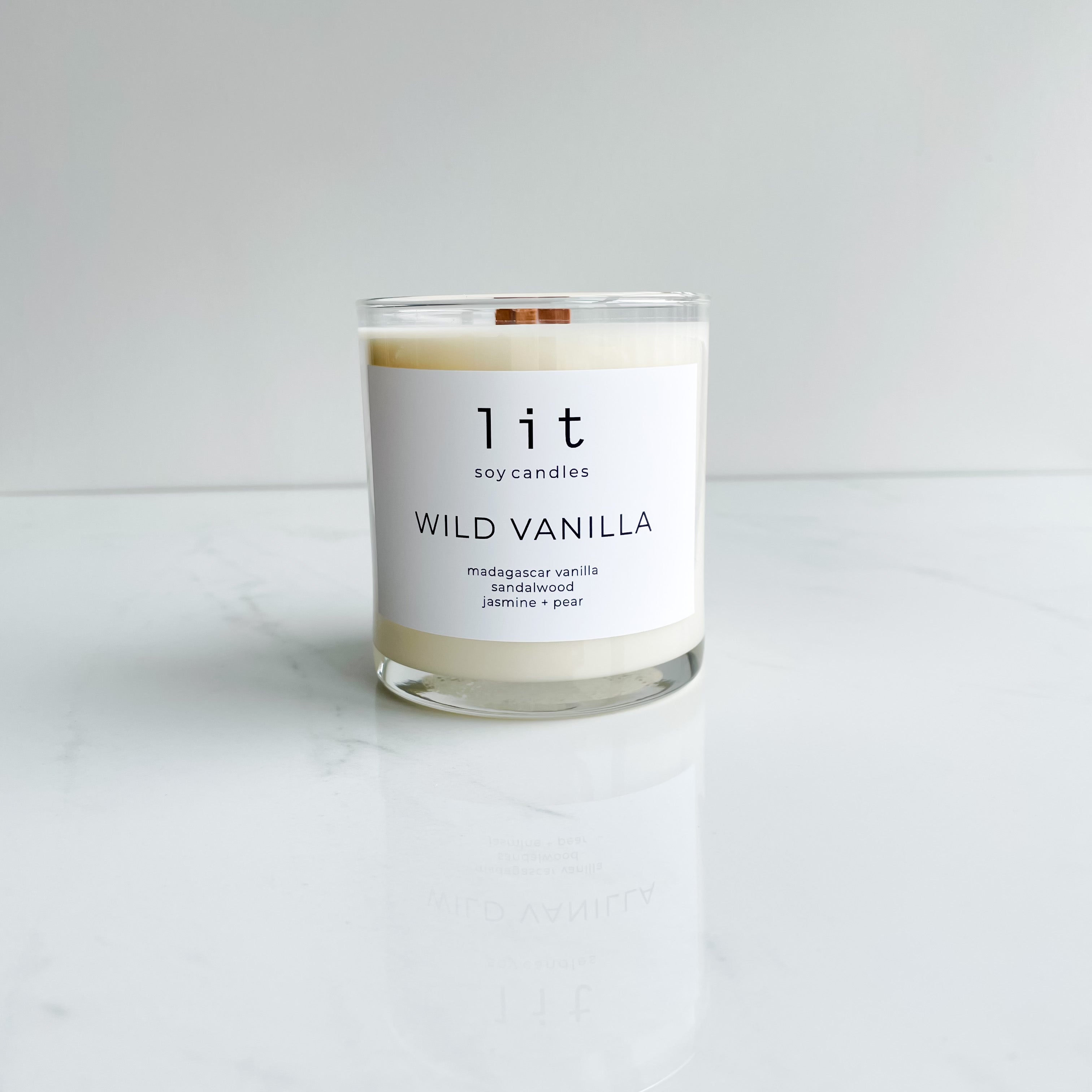 wild vanilla candle  clear glass jar wood wick white label on white marble table