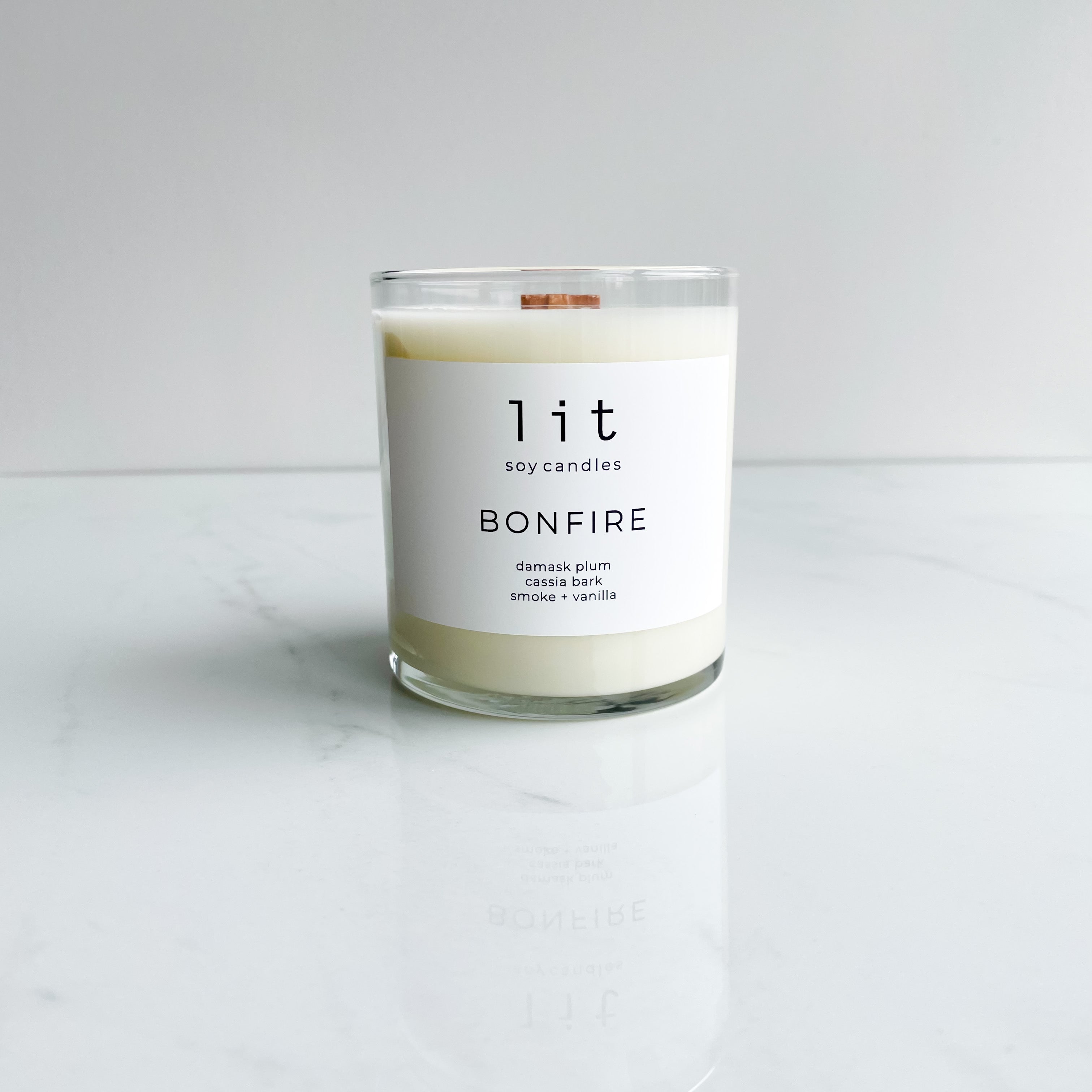 bonfire candle  clear glass jar wood wick white label on white marble table